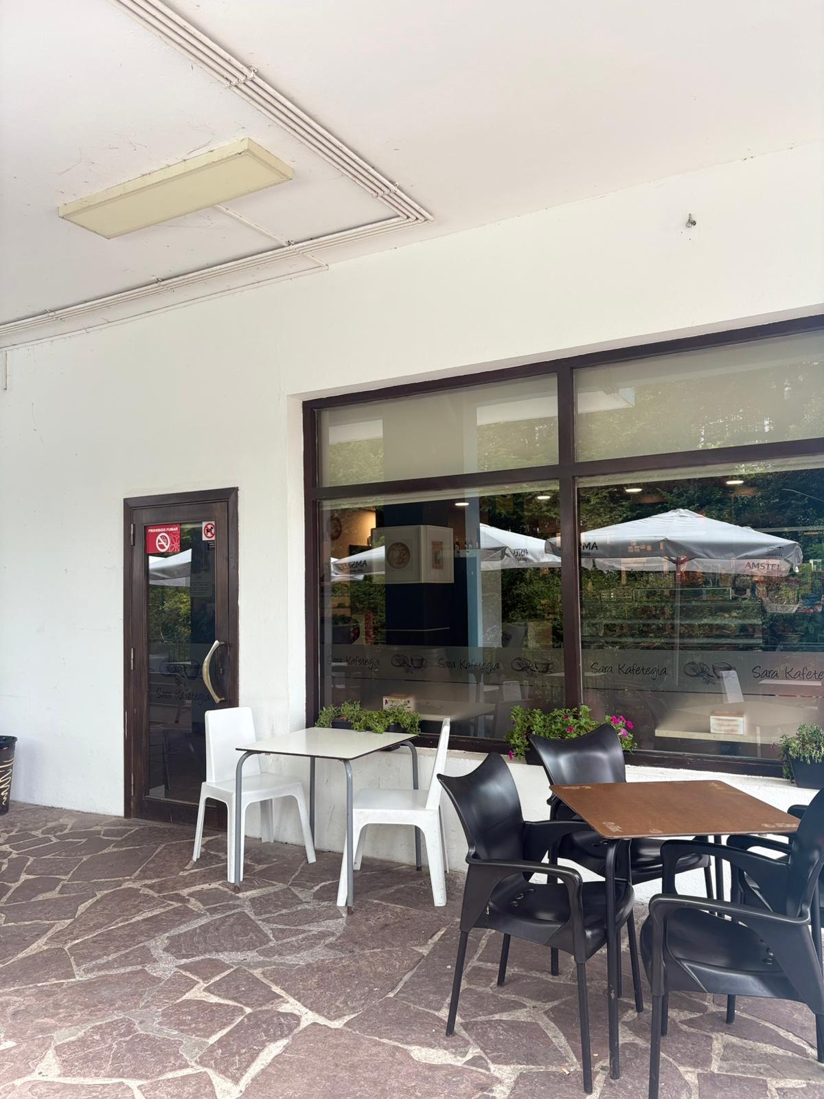 Fachada de Sara Kafetegia con puerta de cristal, terraza con mesas y sillas blancas y negras, y flores en la entrada, en el centro de Bera, Navarra
