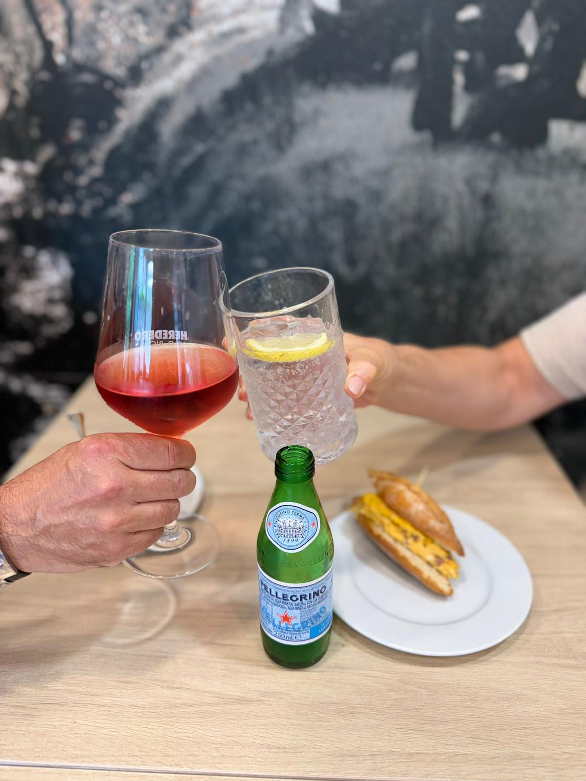 Mesa con brindis de vino rosado y agua San Pellegrino junto a bocadillo de tortilla en la sala interior de Sara Kafetegia
