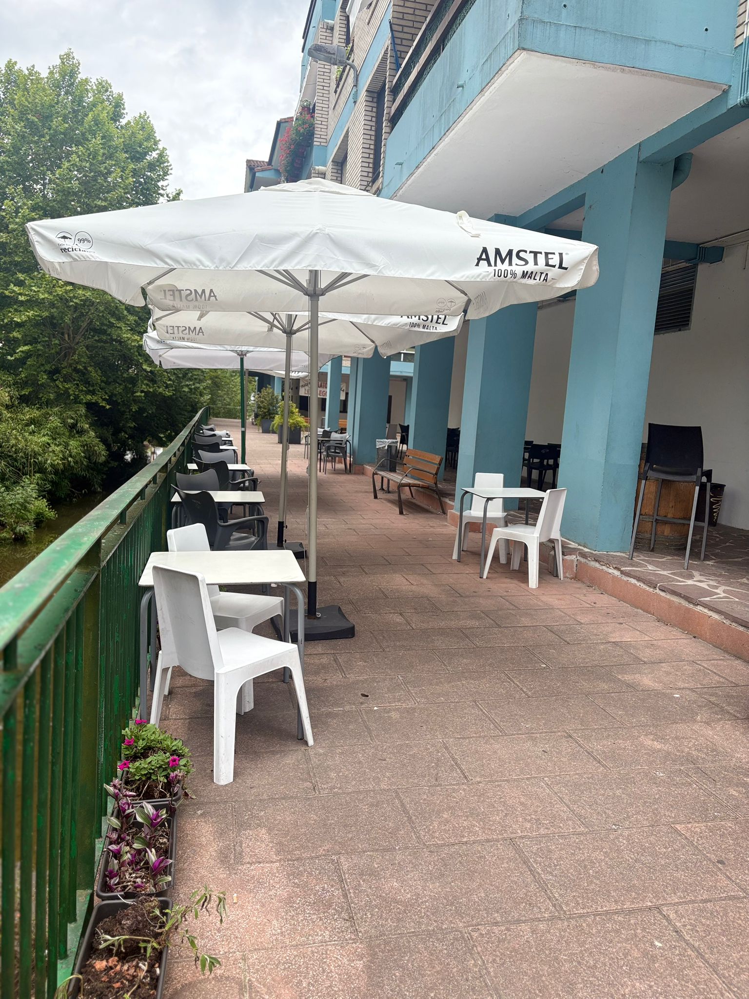 Terraza de Sara Kafetegia con sombrillas Amstel, mesas blancas y flores en jardinera junto al río Bidasoa