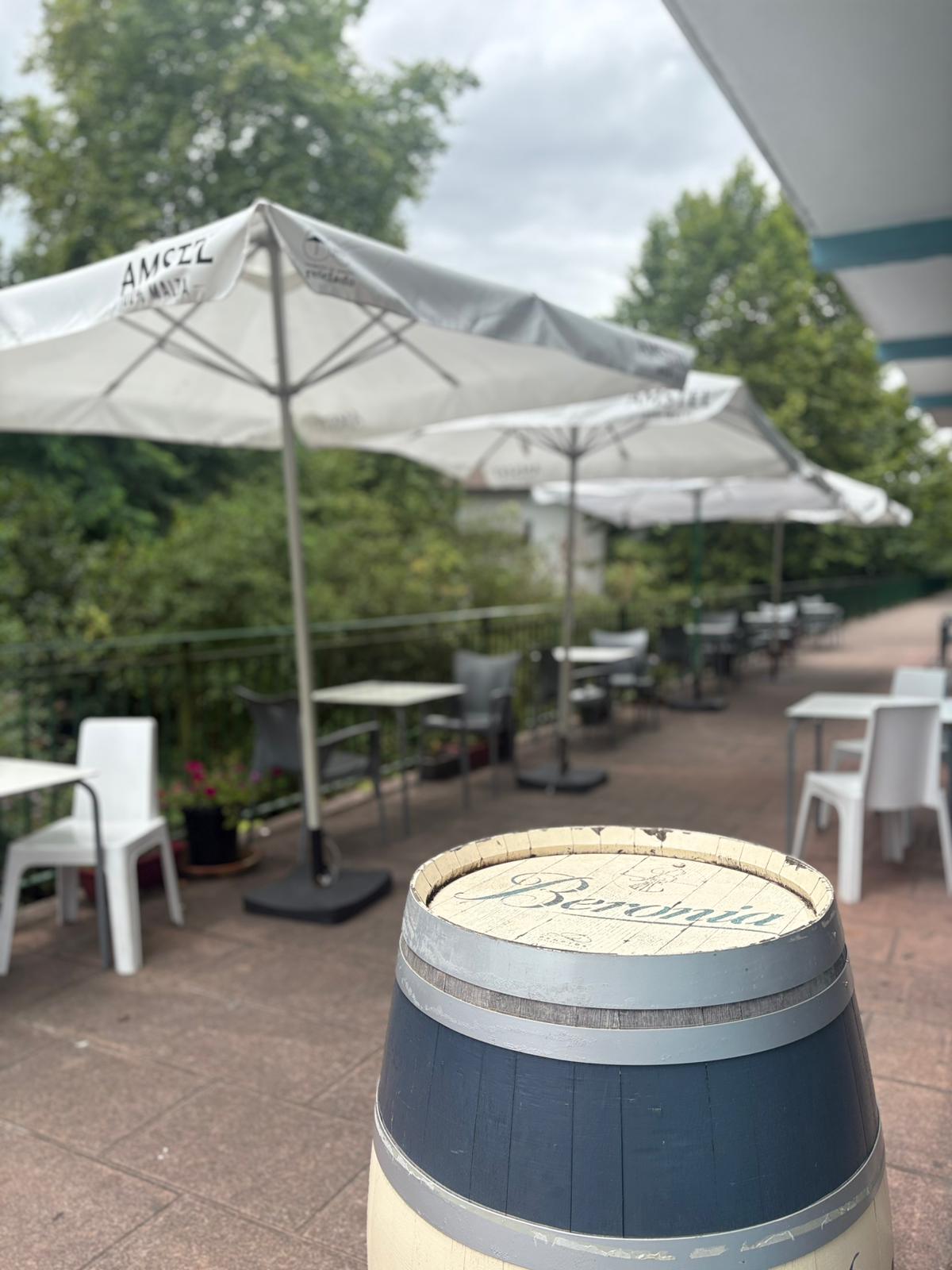 Barrica Beronia decorativa en la terraza de Sara Kafetegia con sombrillas Amstel y arboleda verde al fondo