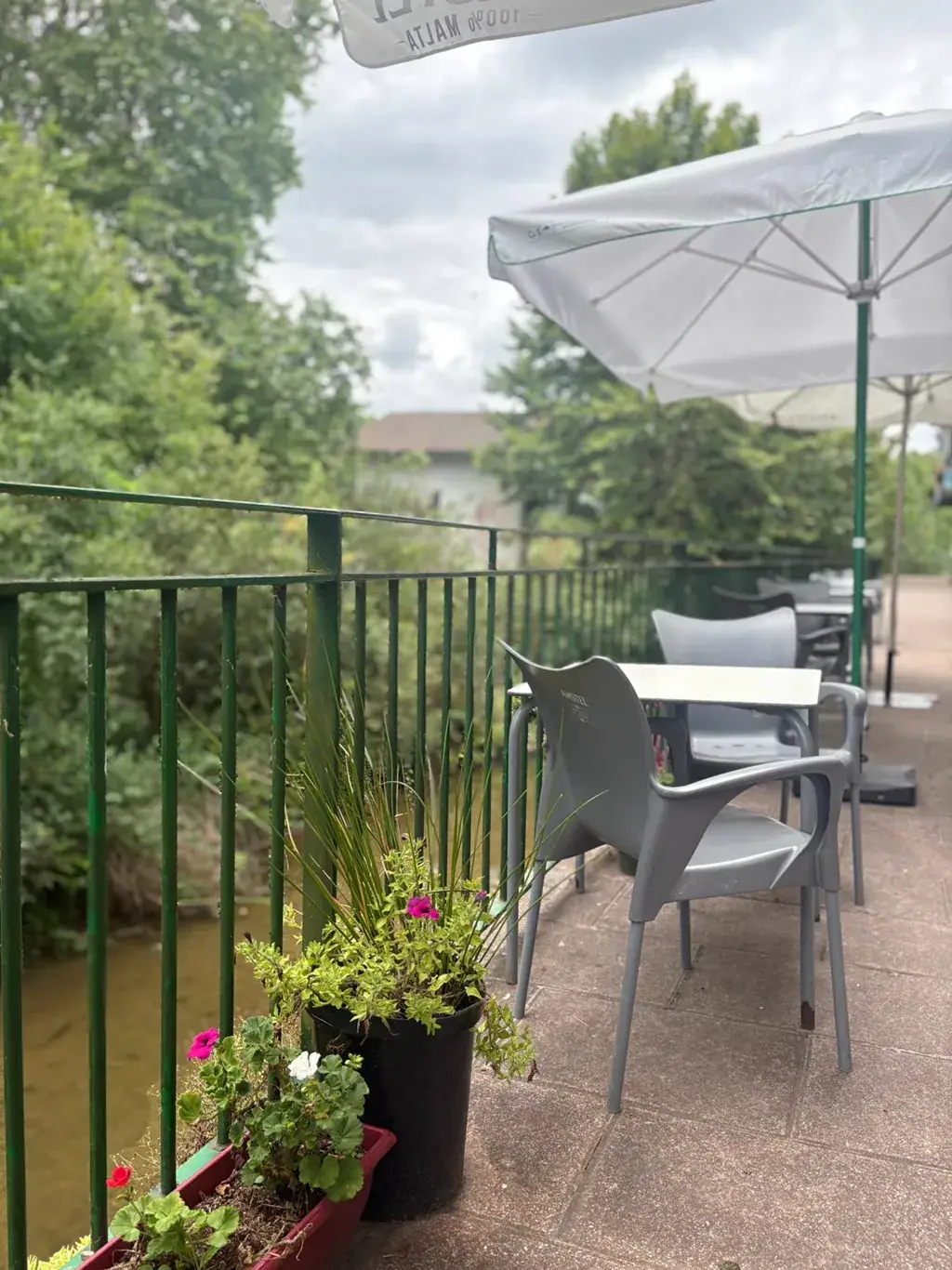 Terraza de Sara Kafetegia junto al río Bidasoa con silla gris, sombrilla, plantas y flores con vistas al agua